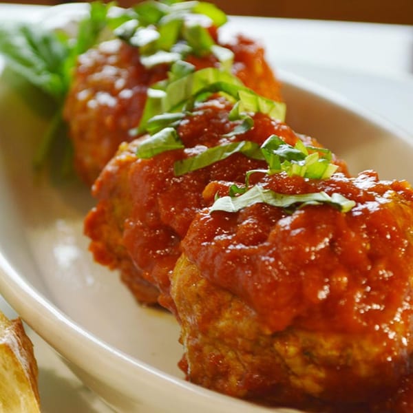 Three Iavarone's Italian meatballs in red sauce, garnished with fresh basil, on a white plate.