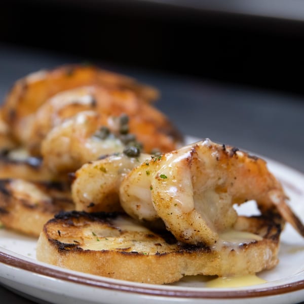 Close-up of grilled shrimp with sauce and capers on toasted bread, an Italian appetizer.