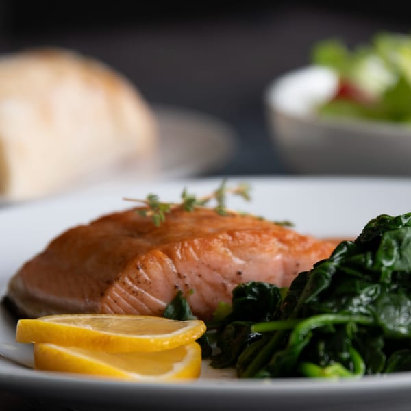 Grilled salmon with spinach and lemon slices, served on a white plate at Iavarone's Steakhouse.