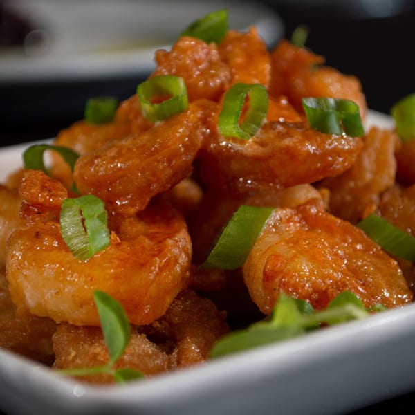 Close-up of crispy fried shrimp coated in a spicy orange sauce, garnished with fresh green onions.