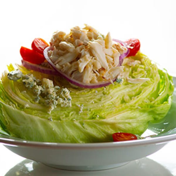 Wedge salad with blue cheese, red onions, cherry tomatoes, and crab meat on a white plate.