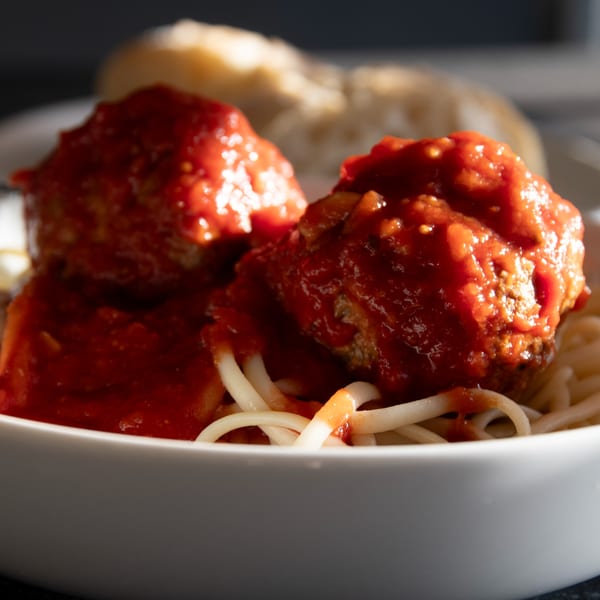 Two large meatballs covered in red sauce on a bed of spaghetti in a white bowl.