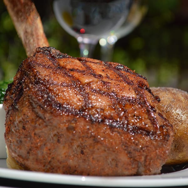 A grilled Tomahawk steak with a bone, served with a baked potato and a glass of red wine.