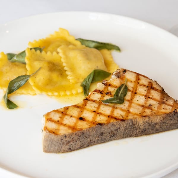 Grilled swordfish steak with ravioli and sage on a white plate at Iavarone's Steakhouse.