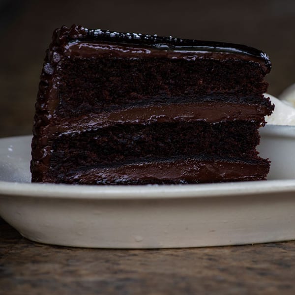 A decadent slice of Iavarone's chocolate cake with rich frosting and powdered sugar on a white plate.